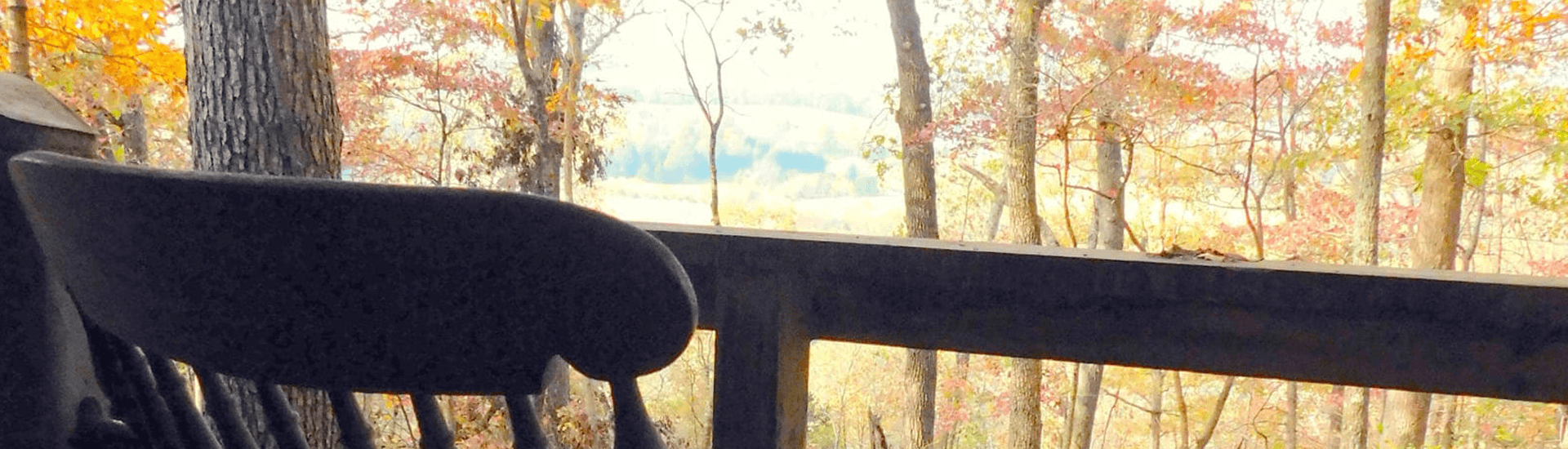 A rocking chair sits on a porch overlooking a forest with autumn foliage.
