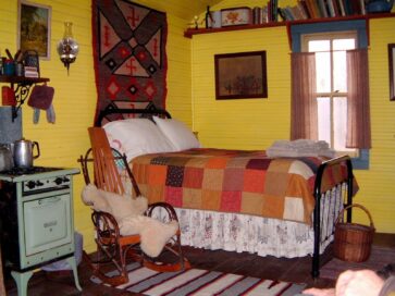 bed in Line Camp Cabin covered with quilty, rocker and old kitchen stove